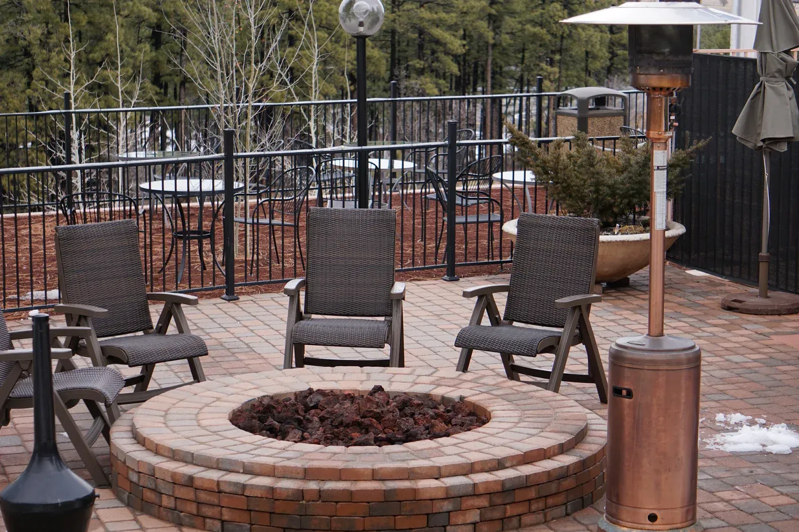 A fire pit on a patio with chairs and a heater.