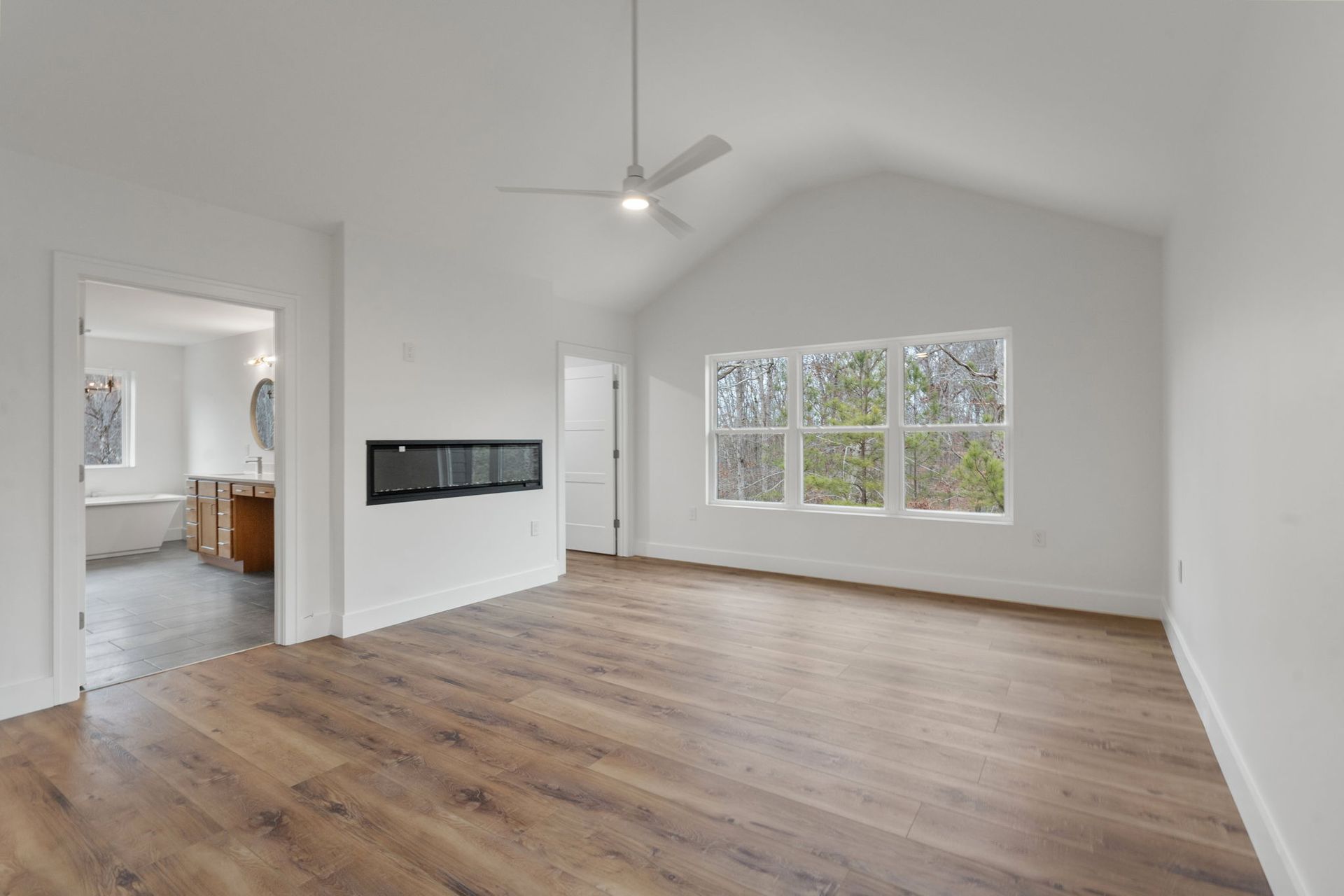 Spacious primary suite with large windows, vaulted ceiling, and fireplace designed by a custom home builder in Chattanooga, leading into a luxury bathroom.