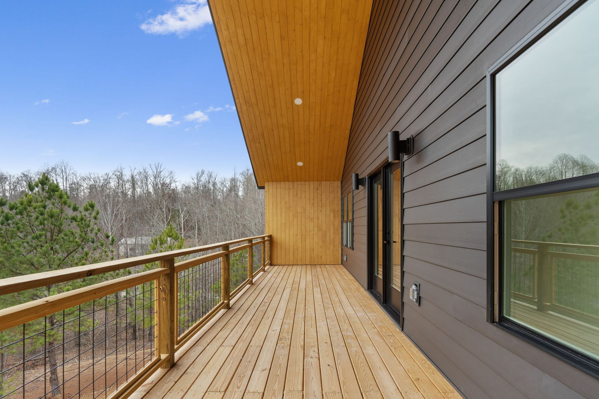 Expansive covered balcony with wood ceiling and railing, surrounded by forest views — crafted by custom home builder in Chattanooga.