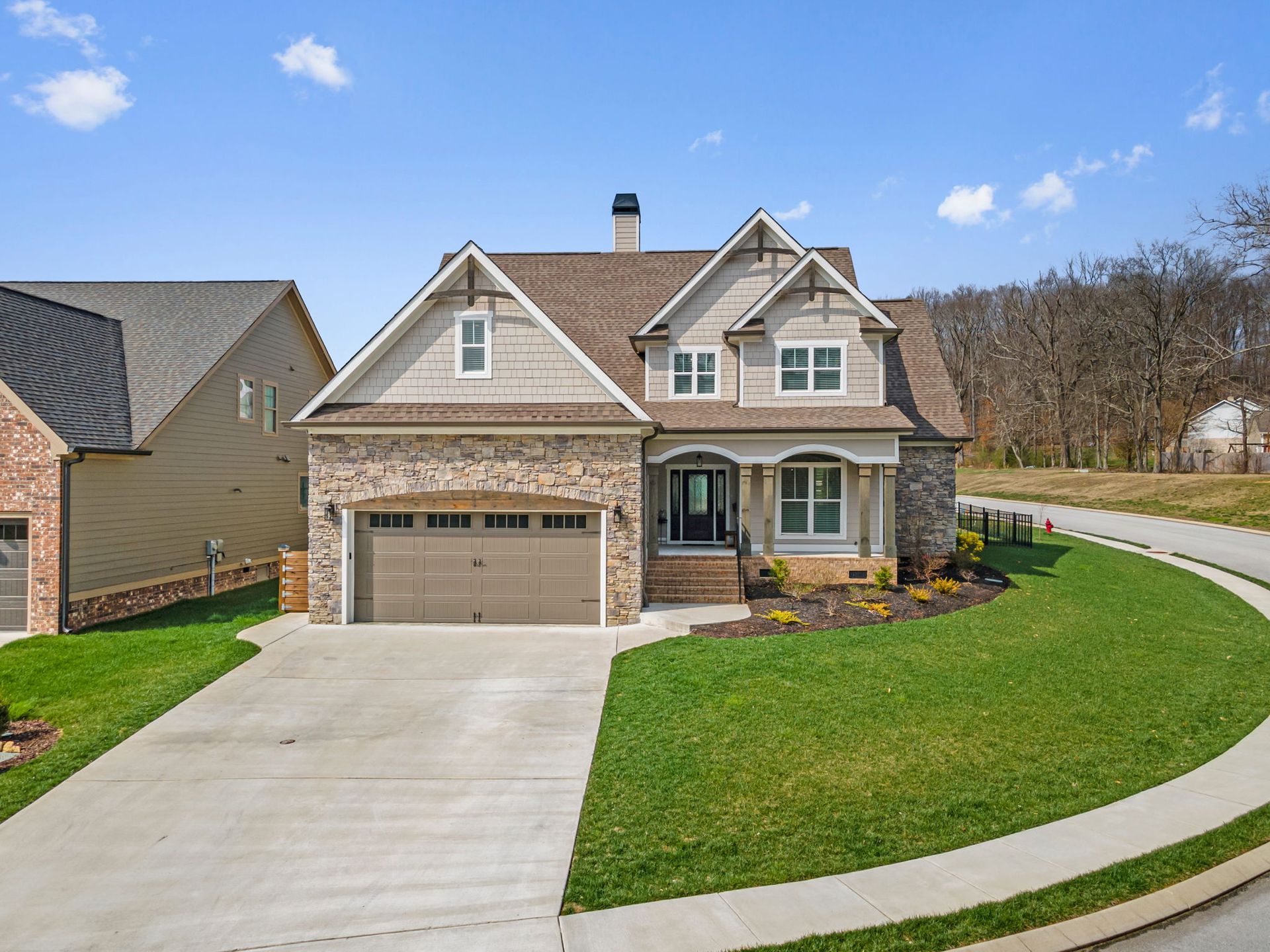 Two-story stone and shingle home with brown garage doors, covered front porch, and curved driveway on manicured corner lot.