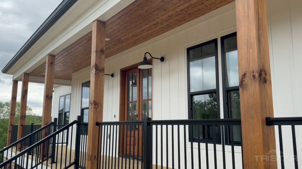 Covered front porch of a modern craftsman home featuring wood columns, board and batten siding, black windows, and metal railing.
