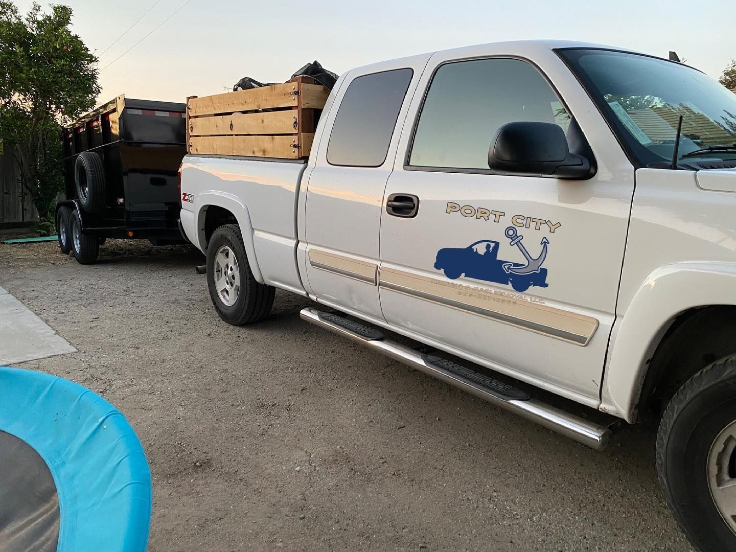 A white truck with a blue truck on the side is parked in a gravel lot.