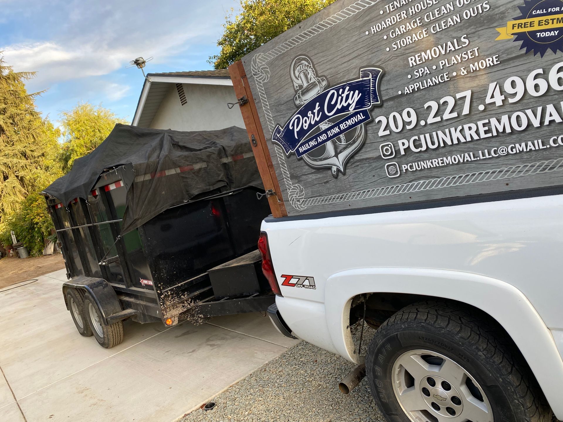 A white truck with a dumpster attached to it is parked on the side of the road.