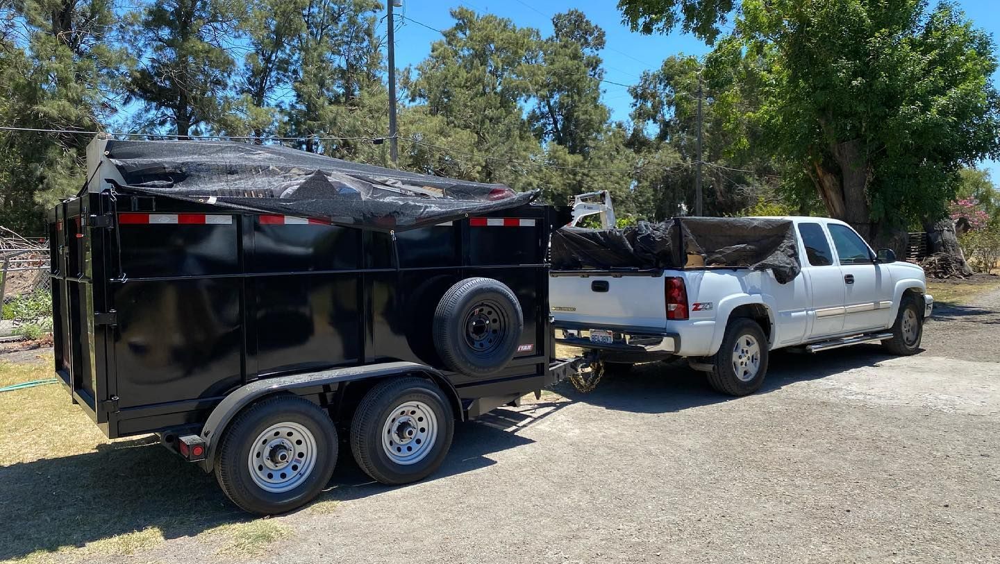 A white truck is towing a black dump trailer.