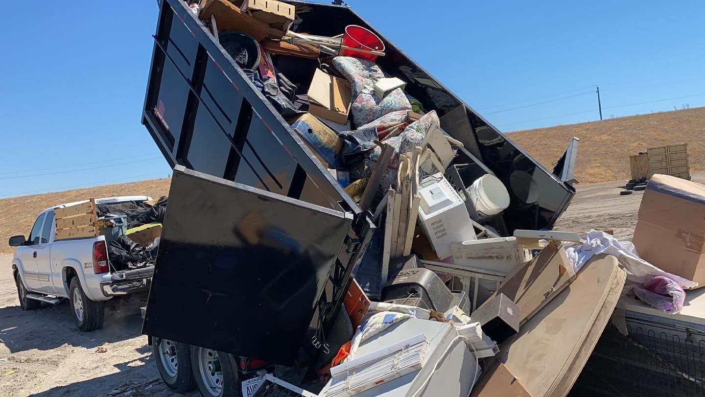 A dumpster filled with lots of trash is sitting on the ground next to a truck.