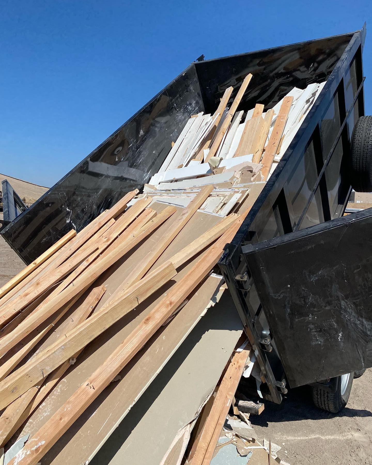 A dumpster filled with wood is sitting on the ground.