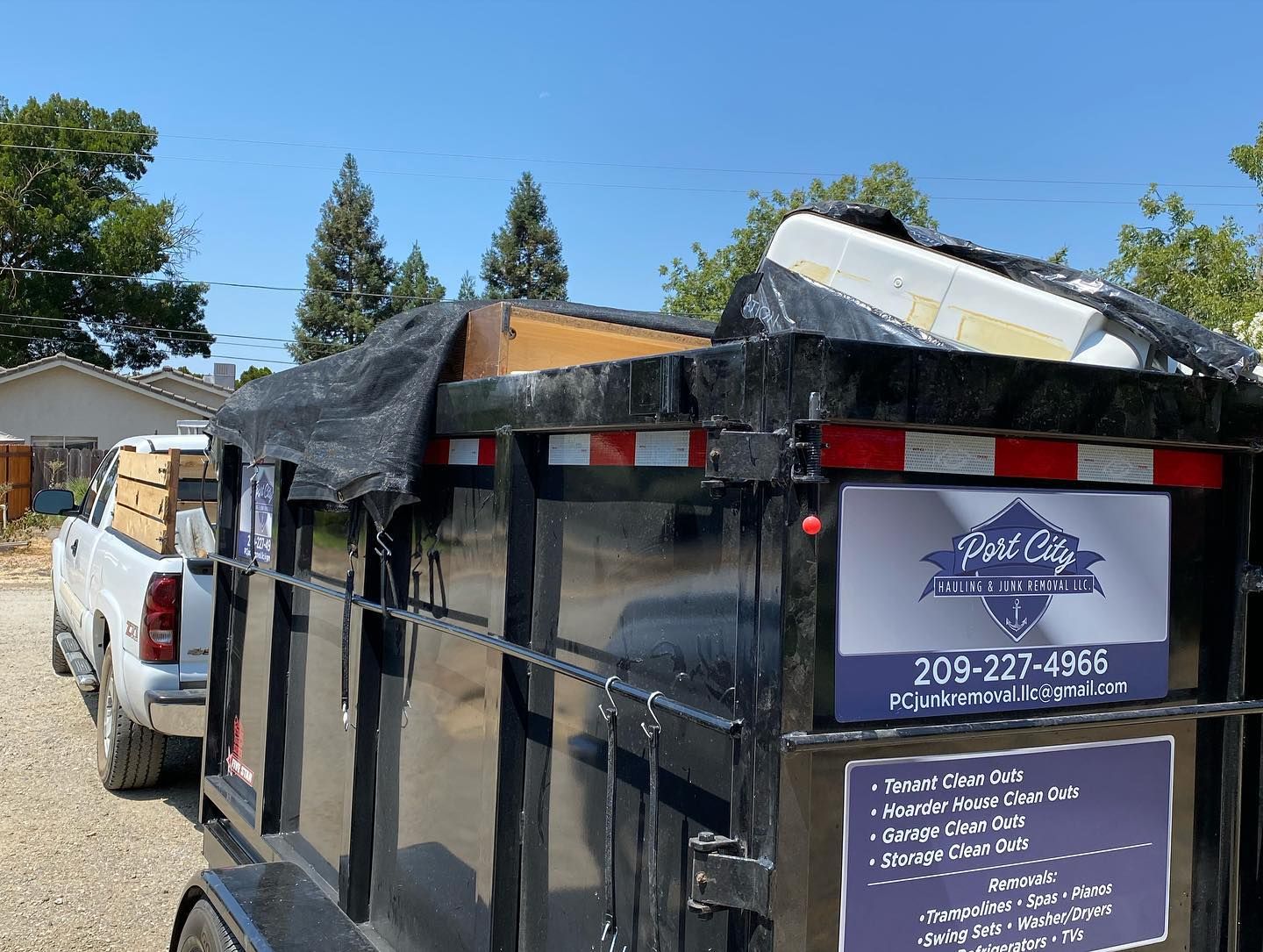 A dumpster trailer is parked next to a truck in a driveway.