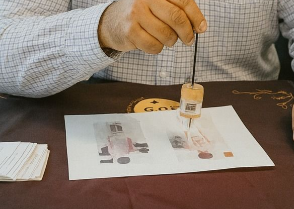 Persona sosteniendo un péndulo sobre una imagen impresa de moneda; una pila de tarjetas está a la izquierda.