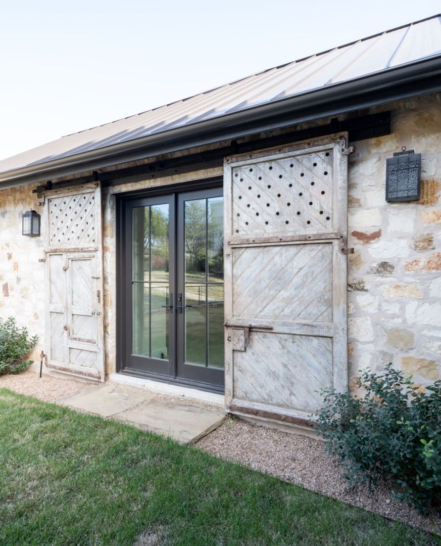 Stone building with glass doors, weathered barn door shutters, and outdoor lighting.