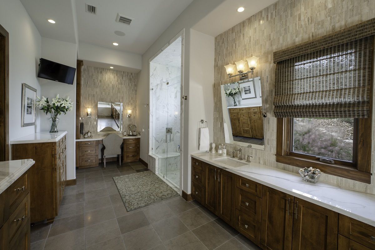 Spacious bathroom with vanity, shower, and window. Brown cabinets, neutral walls, and gray floor.