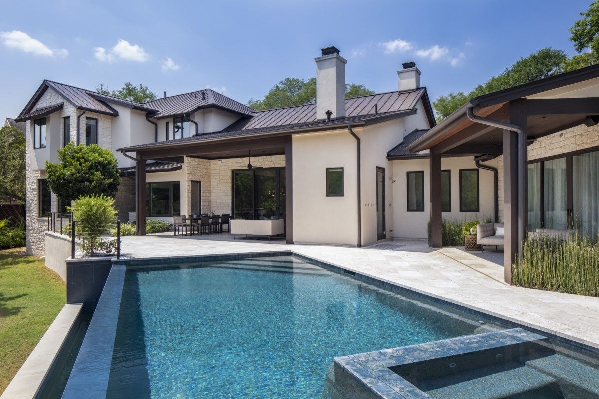 Luxury home with pool. Beige exterior, dark roof, patio, and pool with turquoise water on a sunny day.