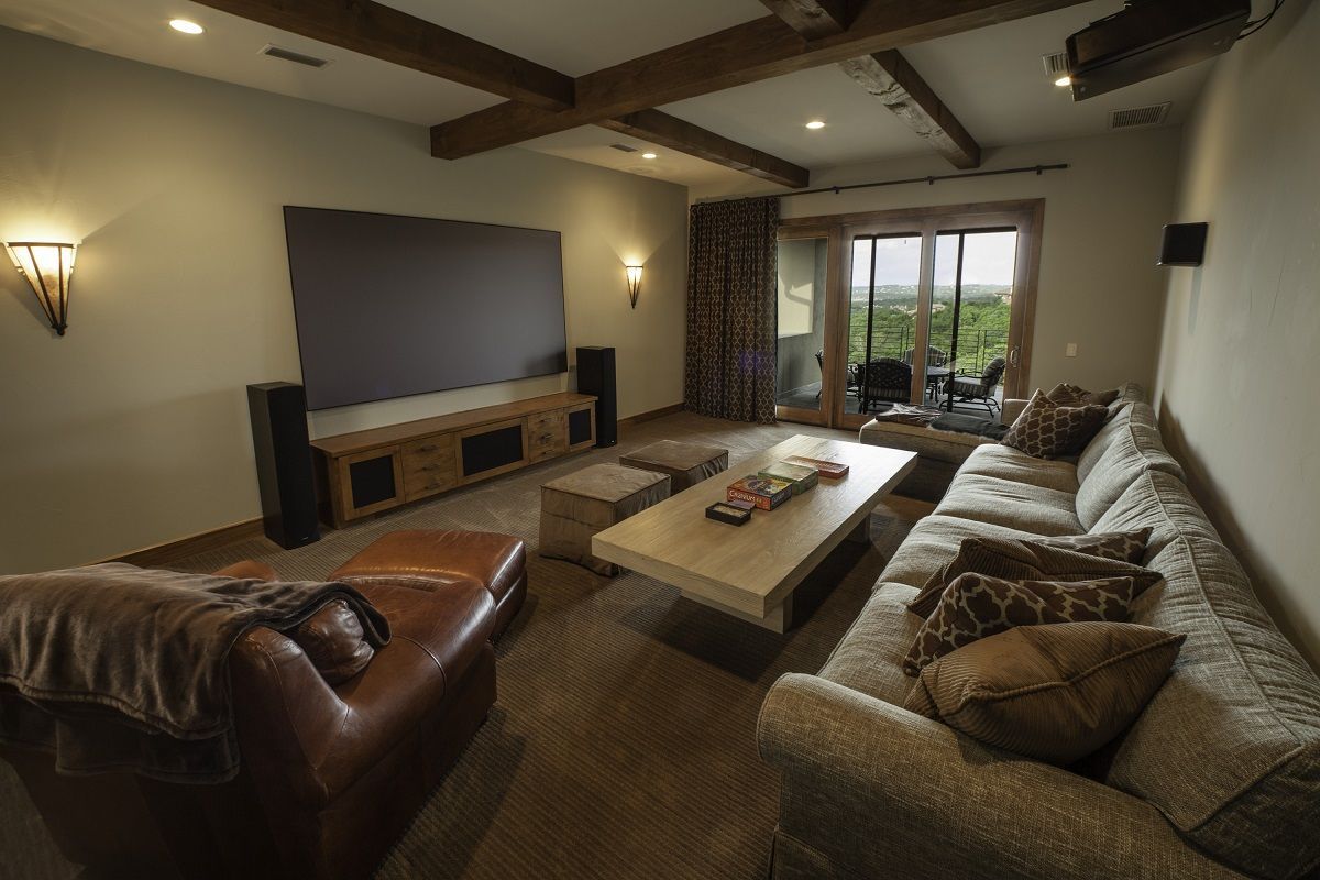 Cozy home theater: large screen, speakers, sectional sofa, leather chair, and sliding doors to outside view.
