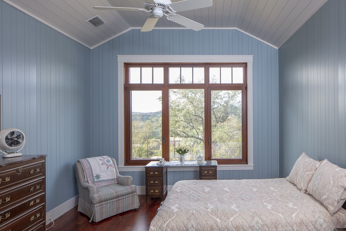 Bedroom with blue paneled walls, dark wood trim, window, and wooden furniture.