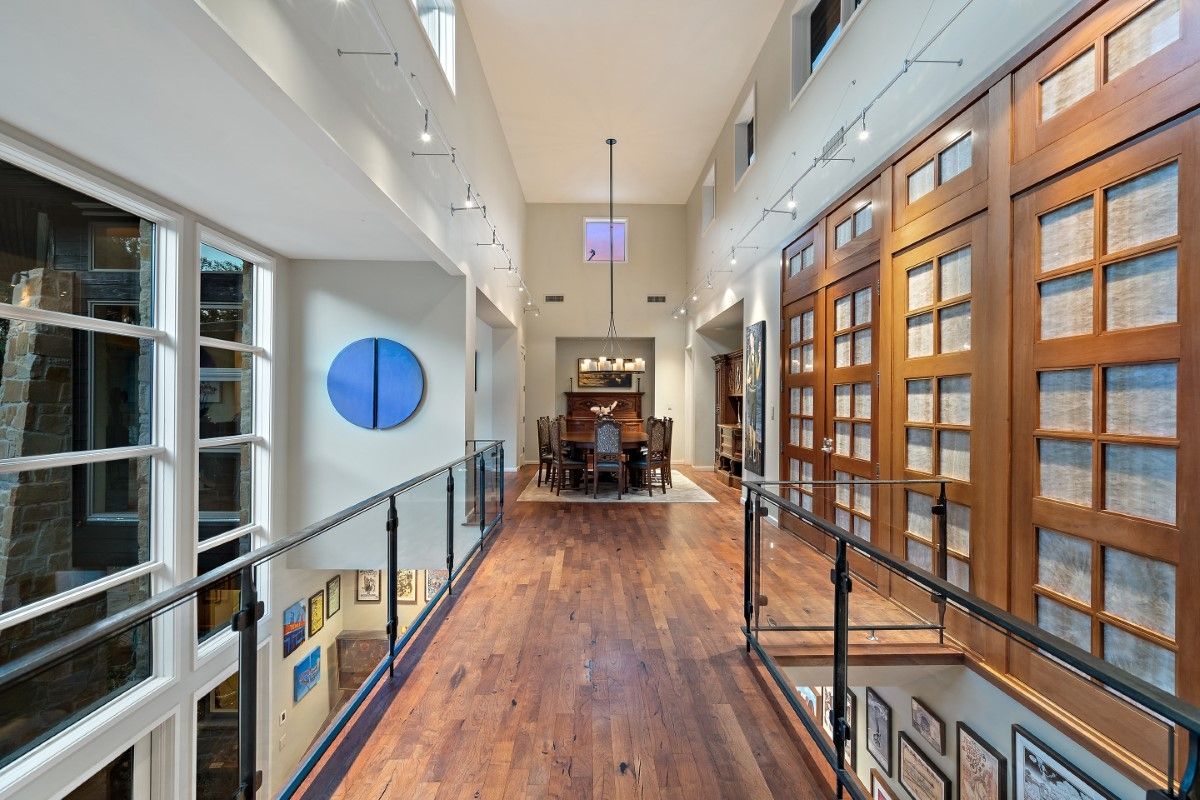 Interior hallway with wooden floors, glass railings, and tall wooden cabinets along the right wall