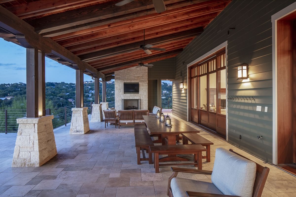 Covered outdoor patio with fireplace, dining table, seating, and view of the landscape.