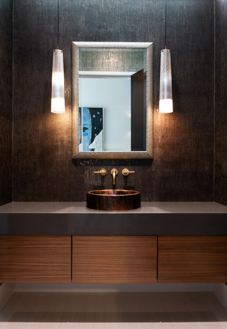 Bathroom with a bronze sink, gold fixtures, wooden cabinet, and a textured dark wall.