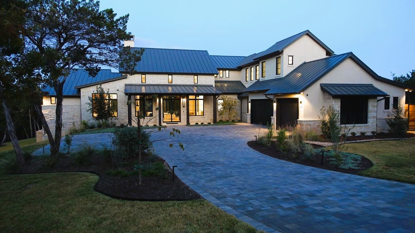 Modern two-story home with a dark blue roof, stone facade, and a long, blue stone driveway.