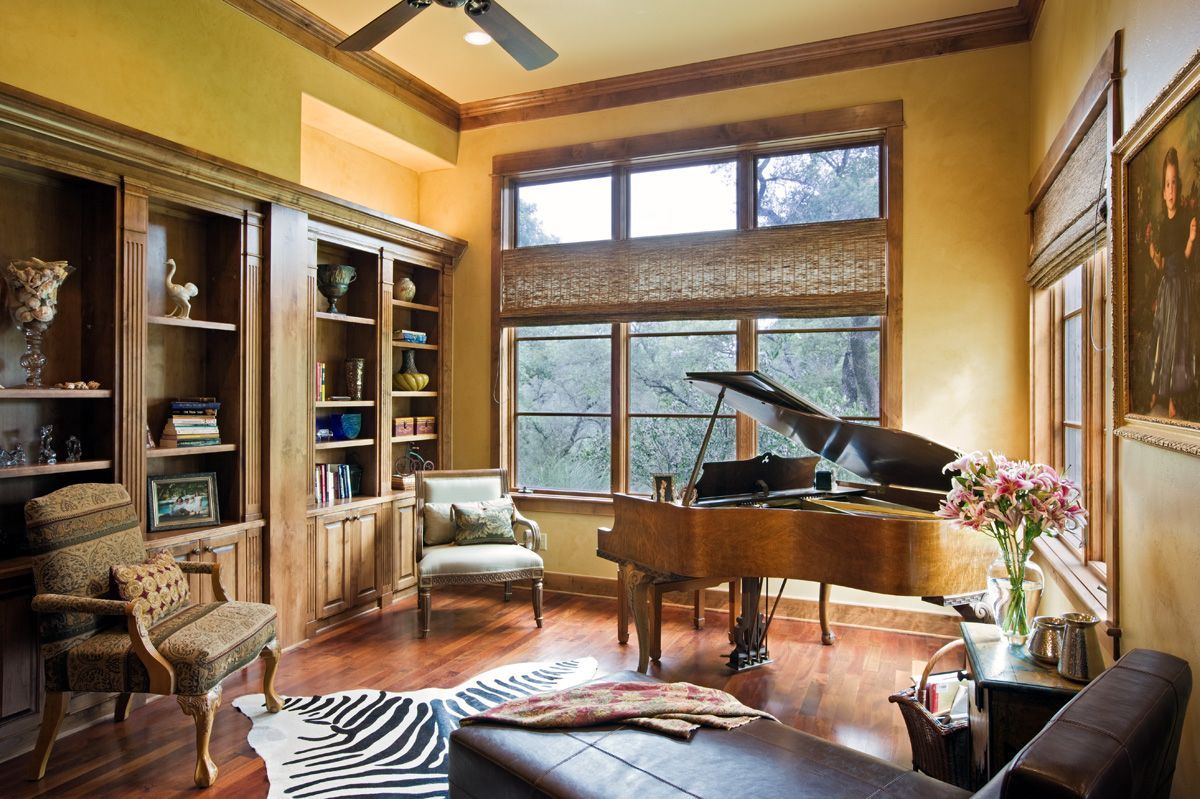 Room with grand piano, built-in bookshelves, zebra rug, and a lounge chair, warm tones.