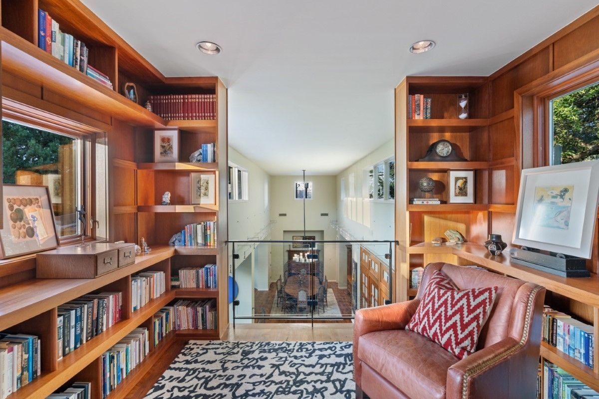 Cozy home library with built-in shelves, a reading chair, and a view to a lower level.