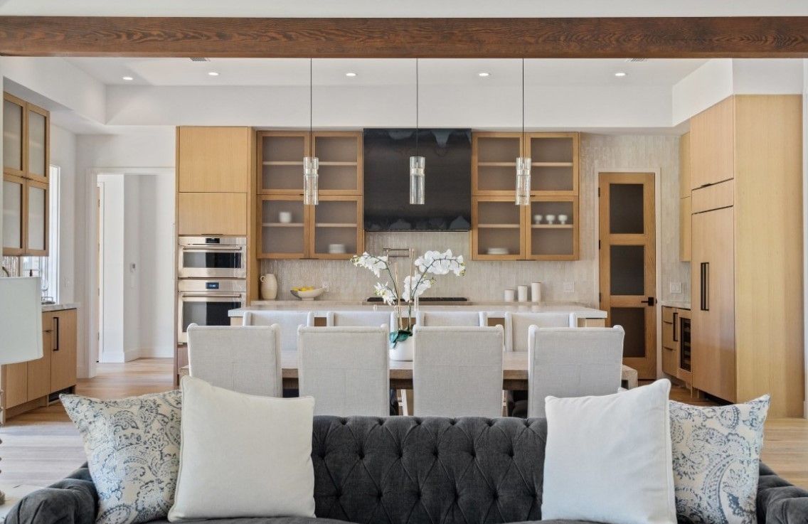 Modern kitchen with a dining area.  Light wood cabinets, white countertops, and a dark grey sofa.