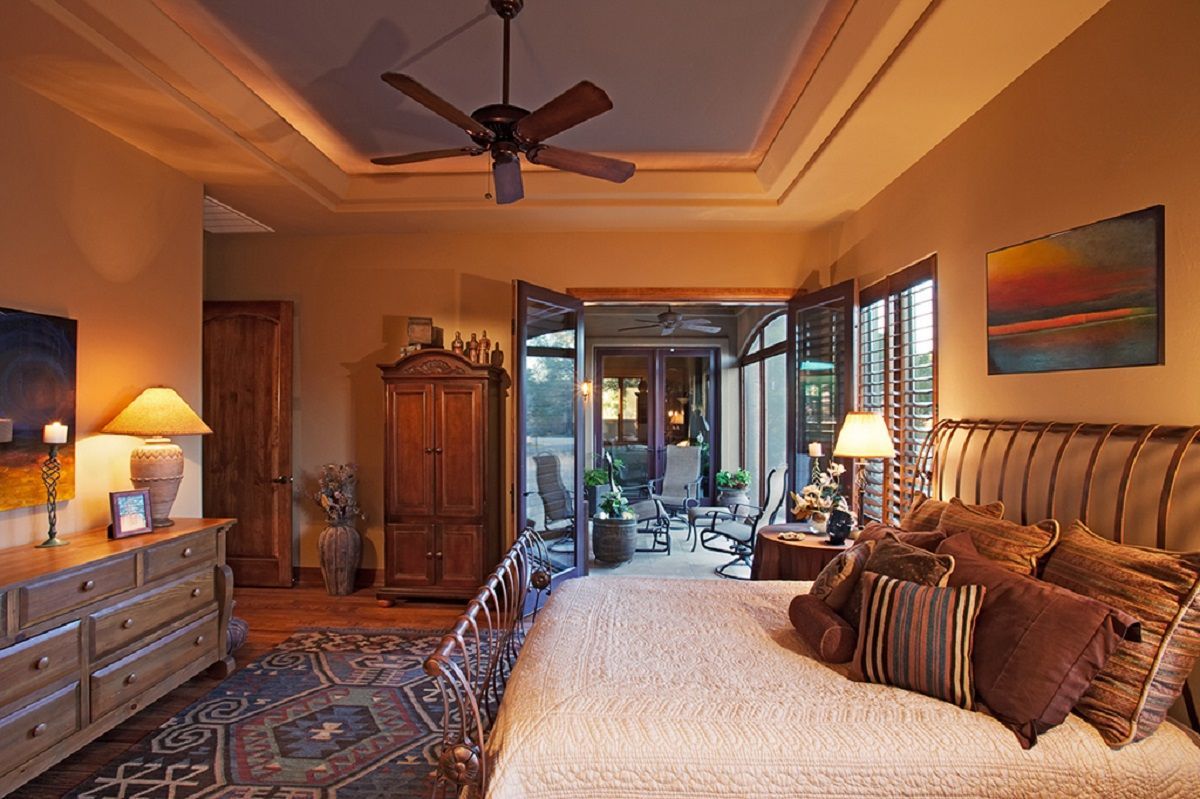 Bedroom with king-sized bed, dresser, armoire, and outdoor patio access. Warm lighting and dark brown furniture.