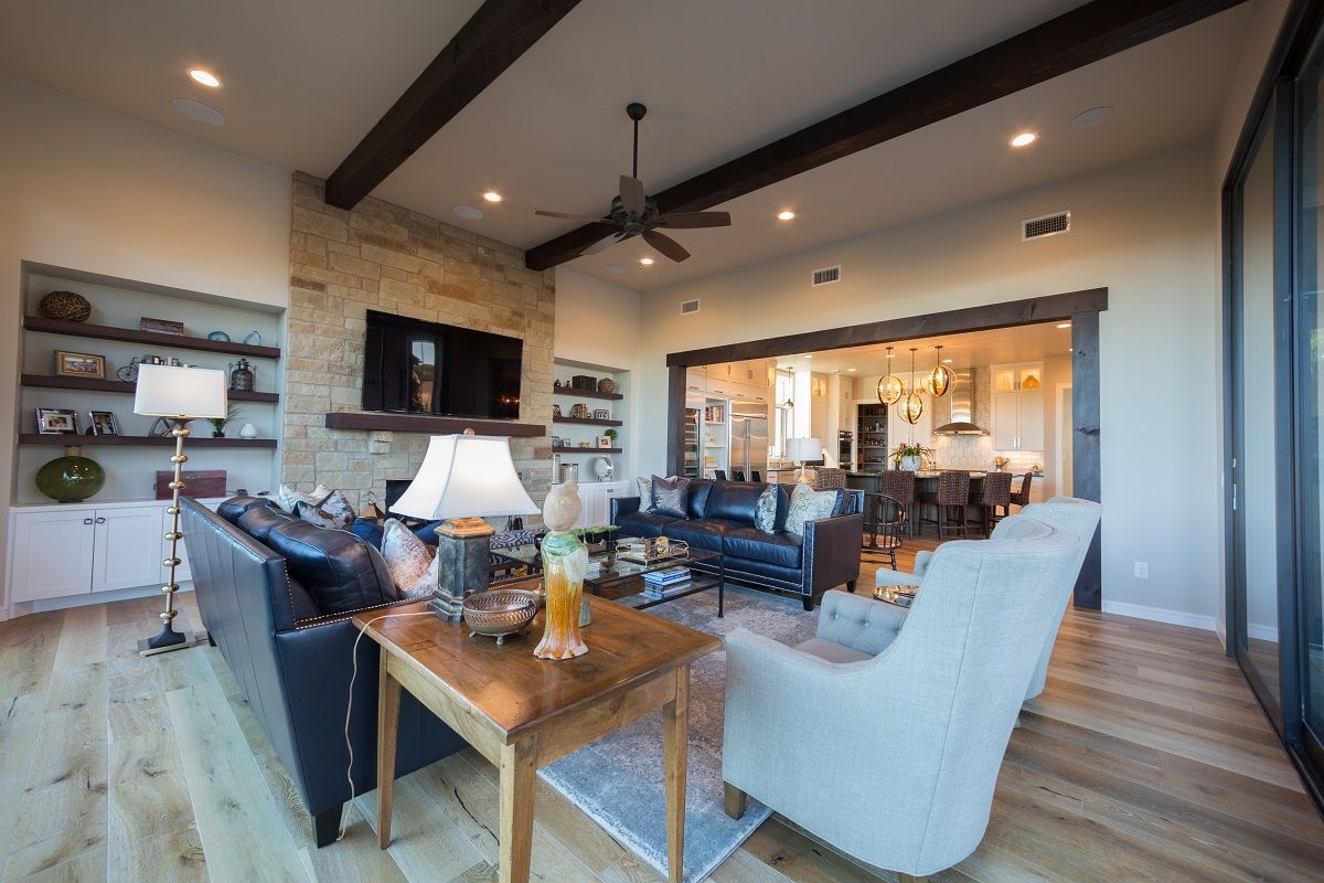 Spacious living room with stone fireplace, leather sofa, white chair, and view of kitchen.