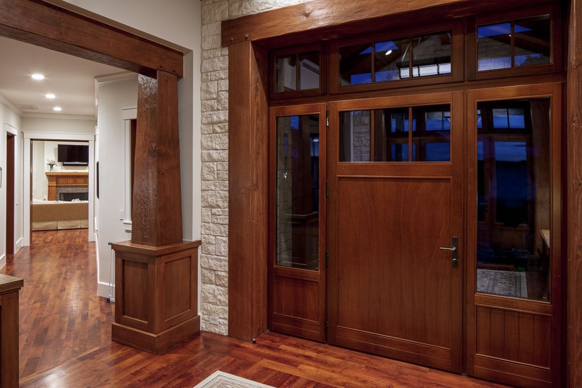 Wooden entry door with sidelights, set in a stone and wood frame, leading into a hallway with a fireplace.
