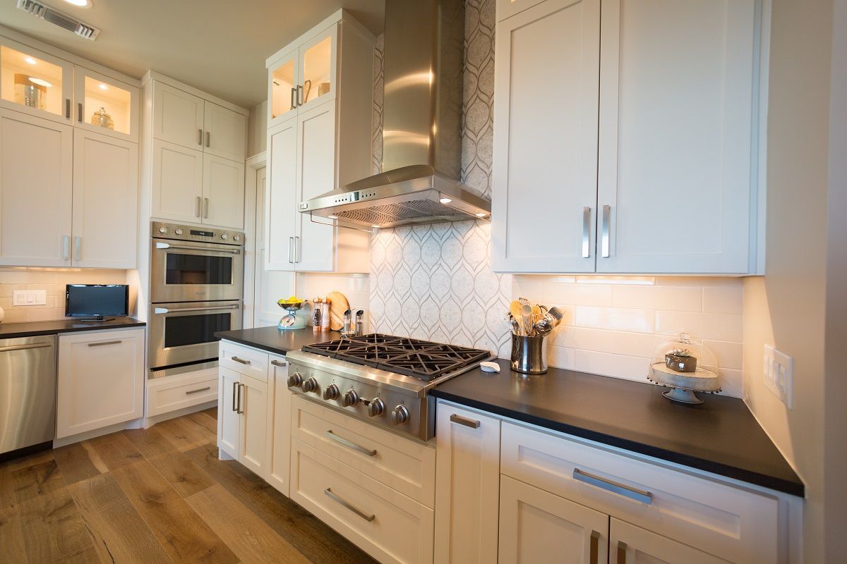 White kitchen with stainless steel appliances, black countertops, and wood floors.