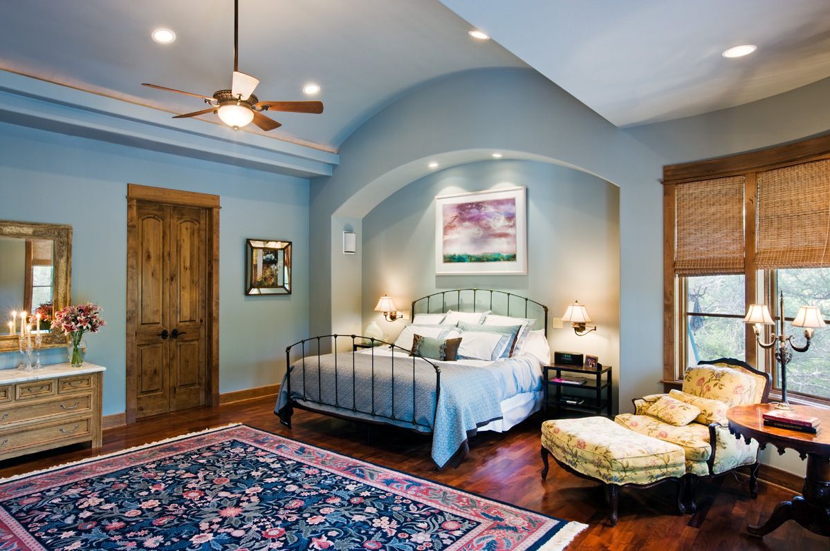 Bedroom with blue walls, arched accent over a bed, rug, chaise lounge, and wood door.