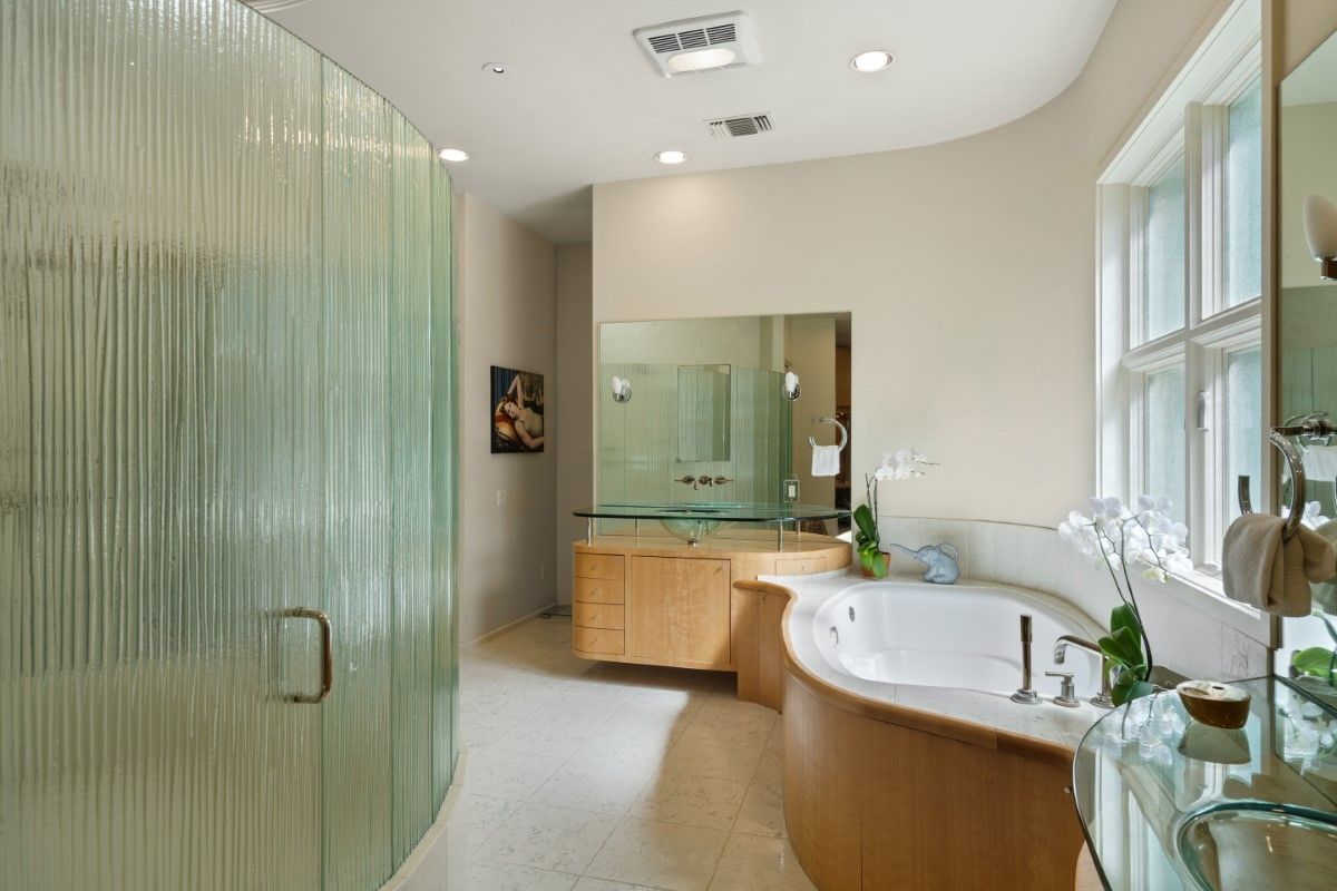 Modern bathroom with a curved shower, bathtub, and vanity. Beige walls, white fixtures, glass accents.