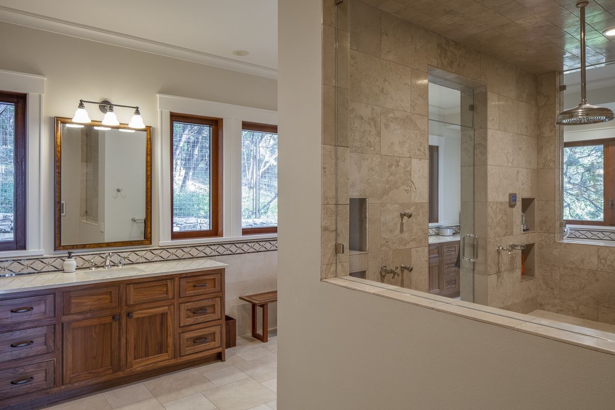 Bathroom with a wooden vanity, beige tile walls, and a glass-enclosed shower.