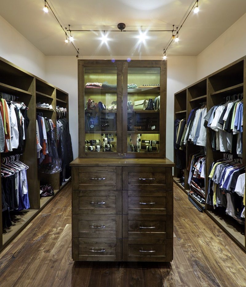 Walk-in closet with dark wood cabinetry and clothing racks. Center island with glass-doored cabinet.