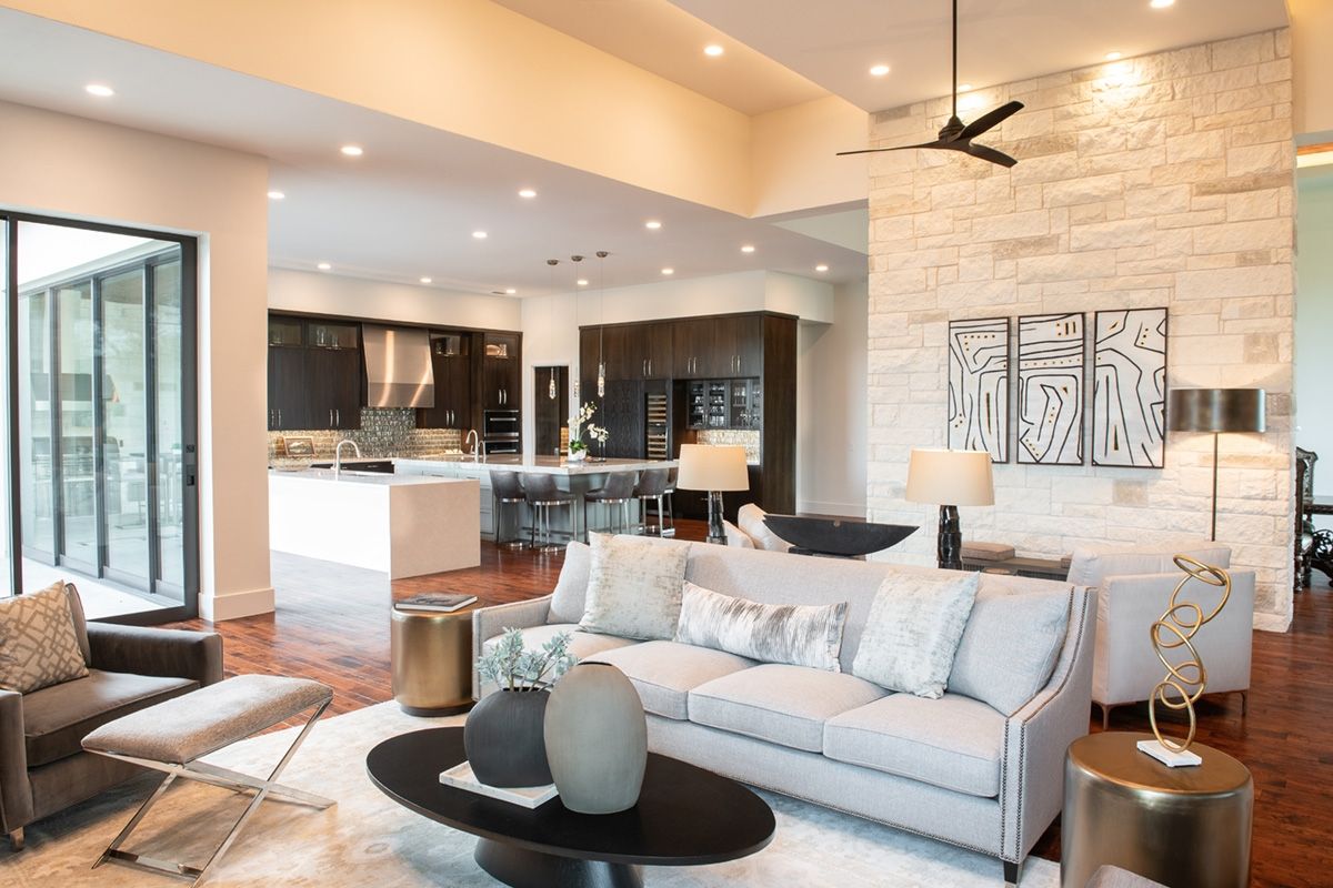 Open-concept living room with gray sofa, gold accents, and kitchen visible in the background.