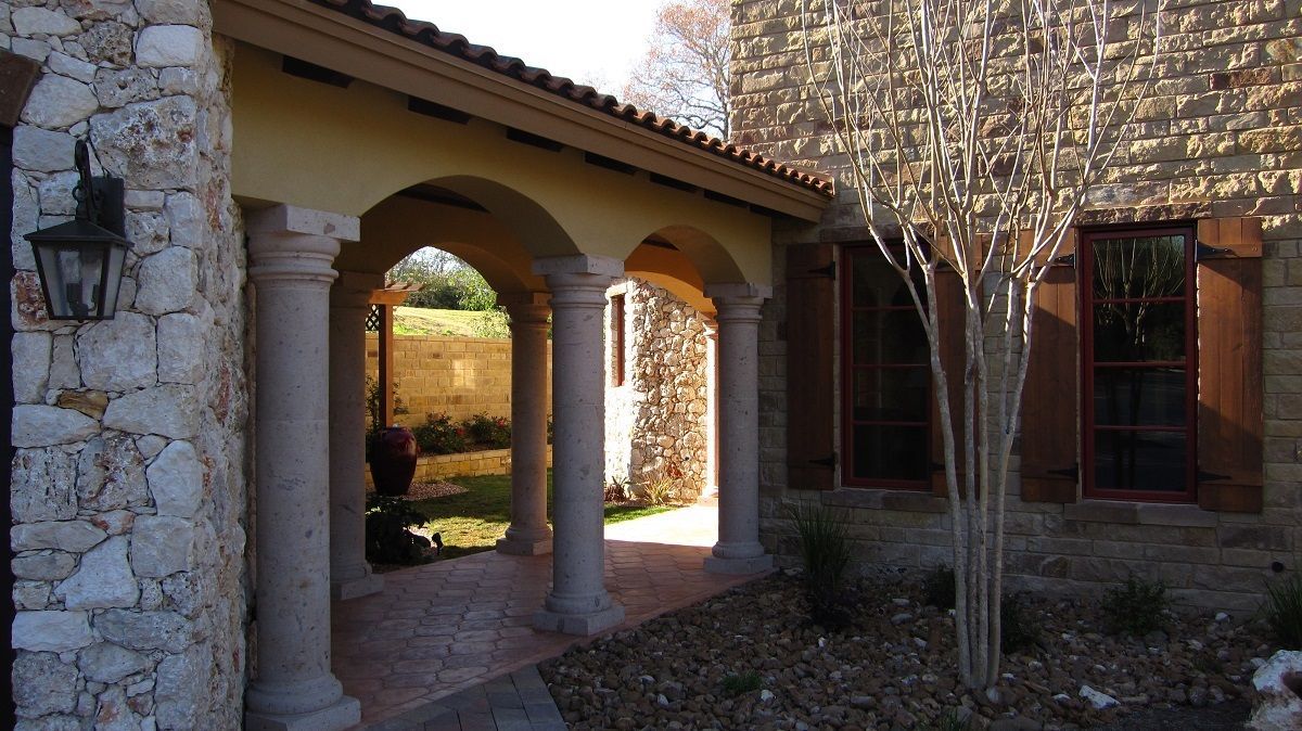 Stone house entryway with arched columns and shuttered windows.