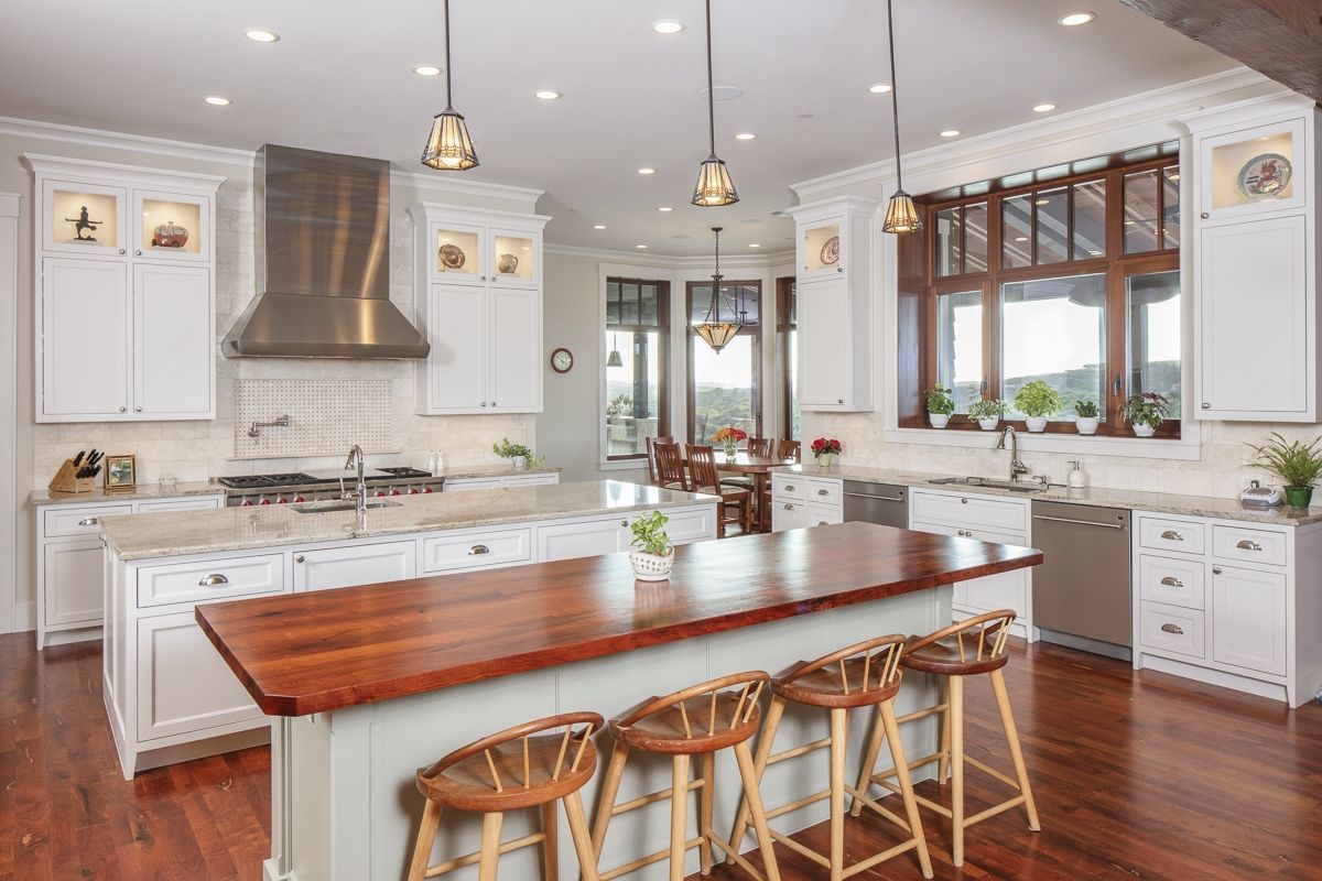 Bright white kitchen with a wood island, a stainless steel range hood, and wood bar stools.