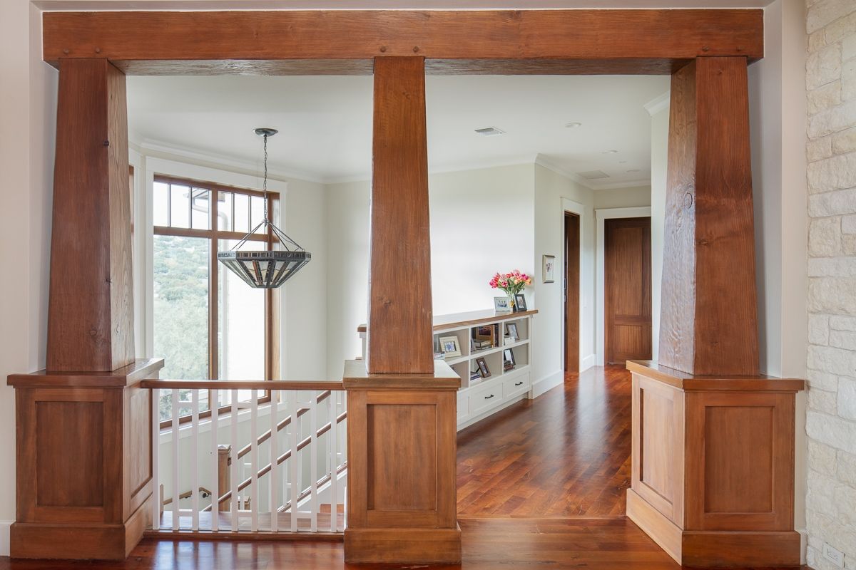 Wooden entryway with columns, beams, and a view of a hallway, stairway, and chandelier.