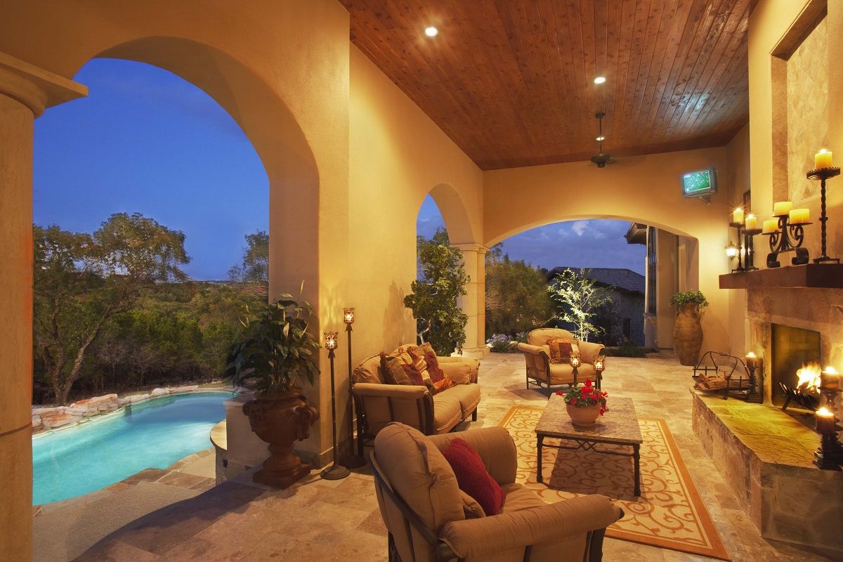 Outdoor patio with arched openings, furniture, fireplace, and a pool; dusk.