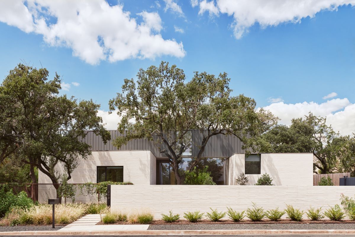 Modern, white stucco home with large tree in front, blue sky with clouds.