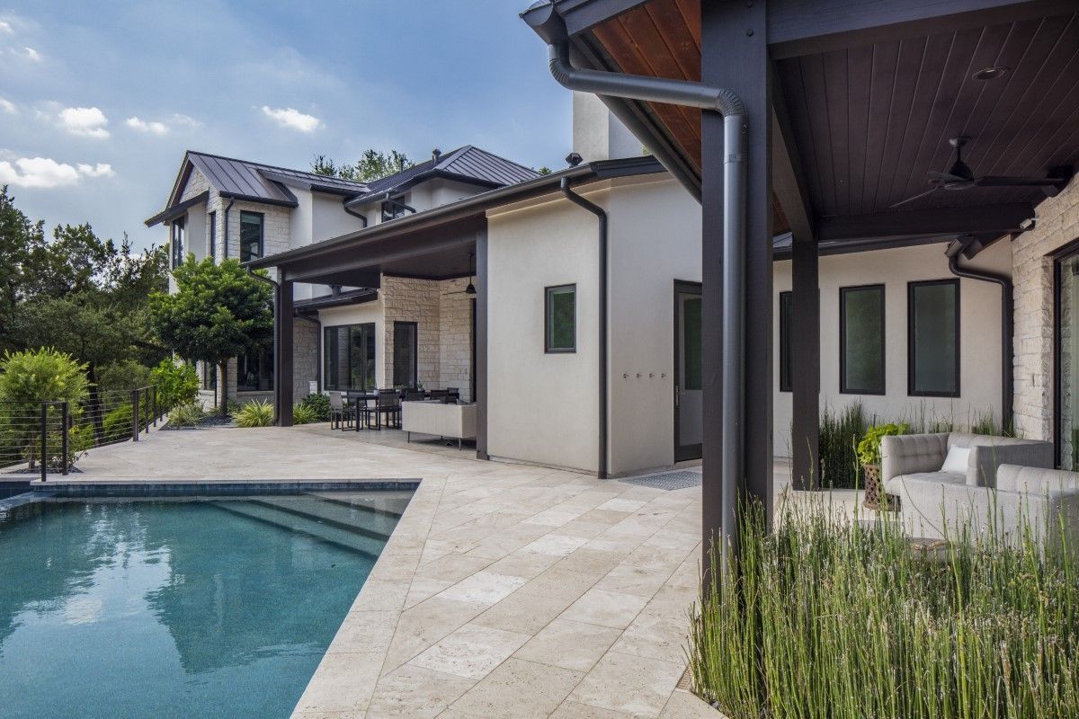 Luxurious home exterior with pool, patio, and lush greenery on a sunny day.