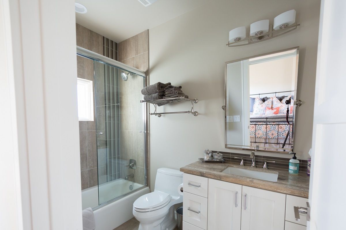 Bathroom with a glass shower, toilet, vanity, and mirror. Light beige walls and white cabinets.