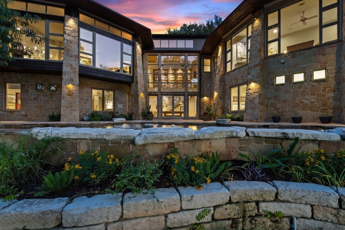 Stone mansion exterior with large windows, a pool, and a sunset sky.