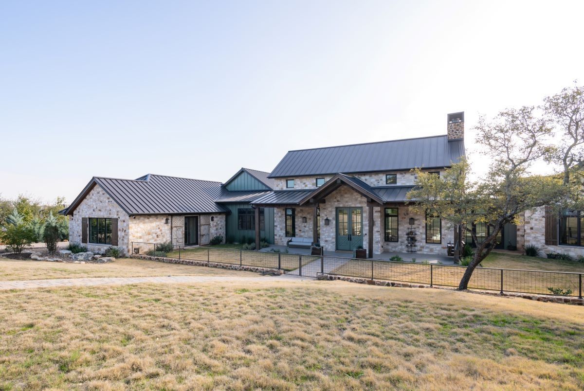 Stone farmhouse with metal roof, surrounded by grassy field under a clear sky.