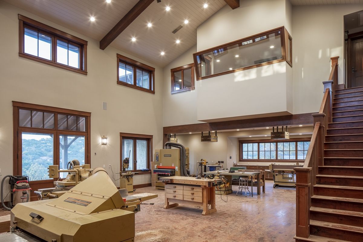 Spacious woodworking shop with natural light, tools, wooden beams, and staircase.
