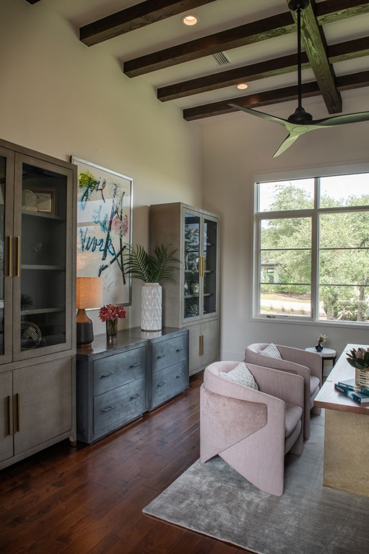 A modern office with light pink armchairs, a wooden desk, and large windows overlooking greenery.