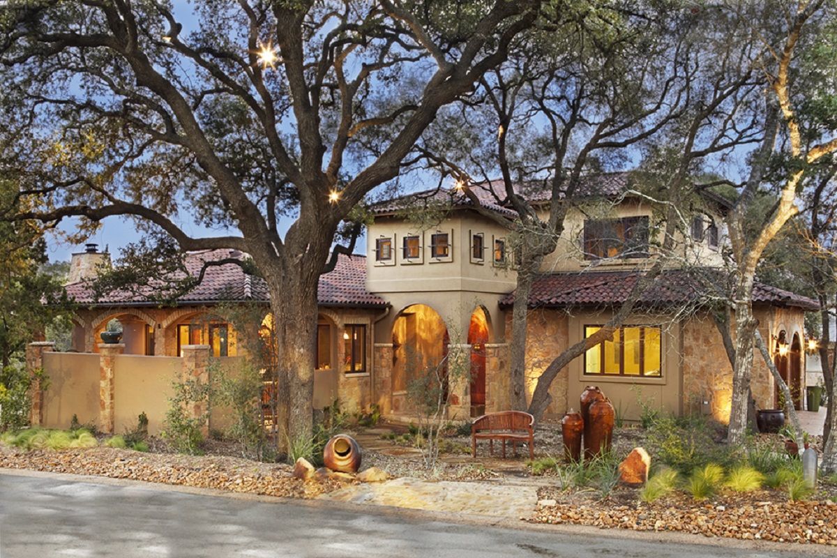 Spanish-style home with arched entryway, red tile roof, and oak tree in front.