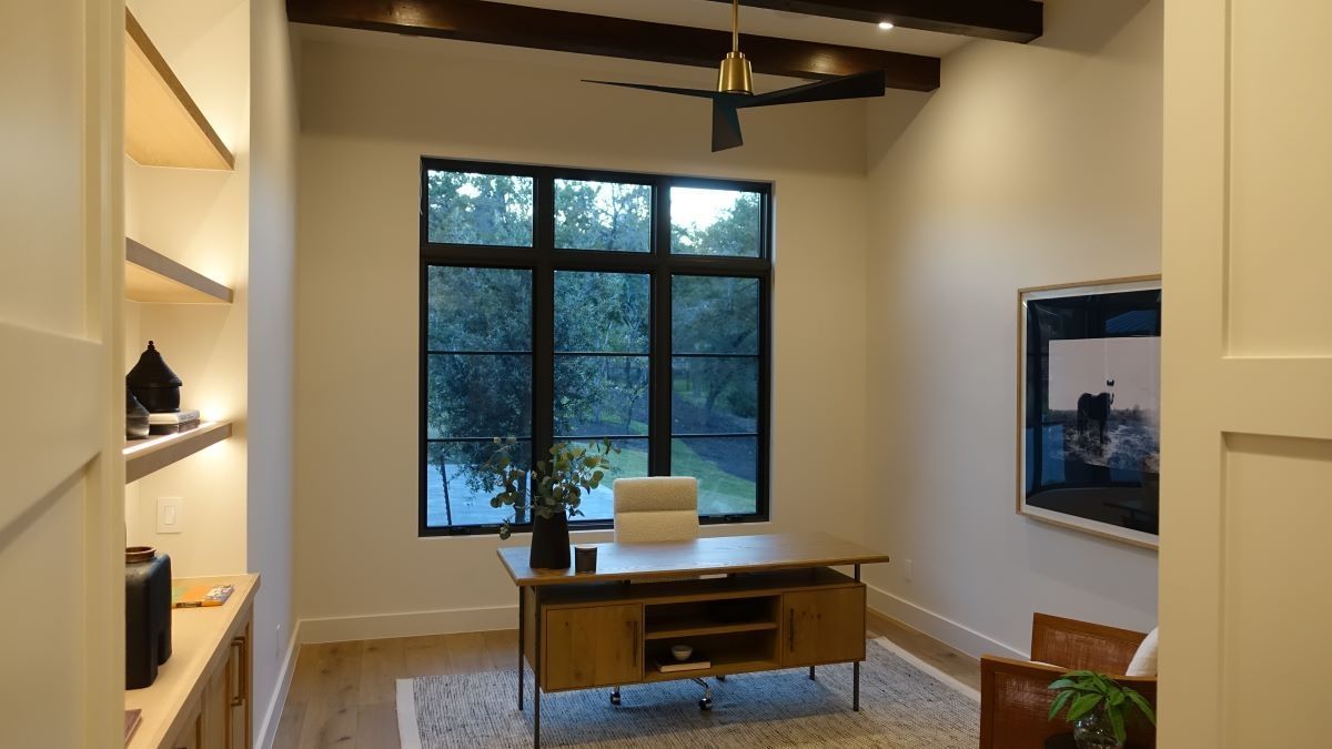 Home office with a desk by a large window, shelves, and an abstract painting.