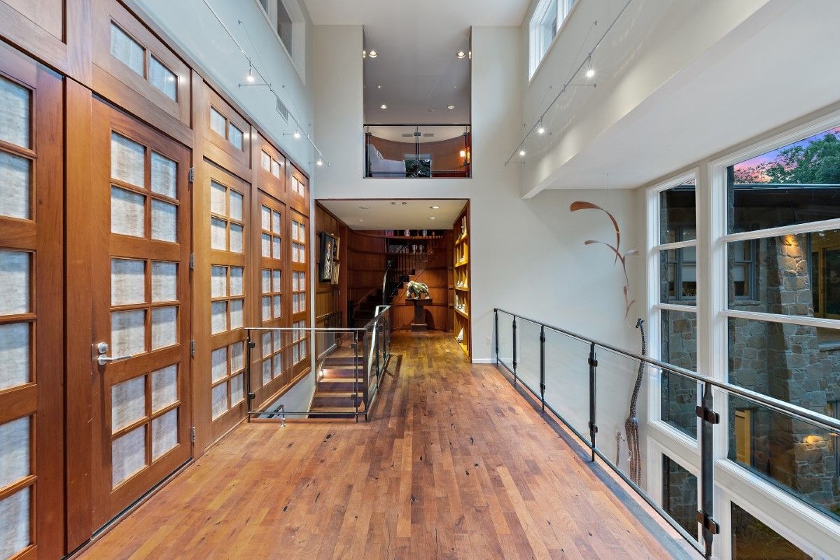 Wooden-floored hallway with tall glass windows and wooden doors, looking towards a room with a staircase.
