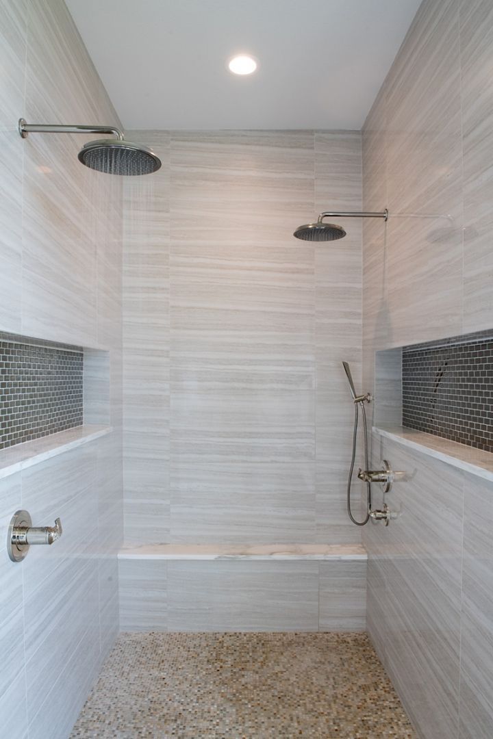 Modern shower with stone floor, two shower heads, bench, and tiled walls.