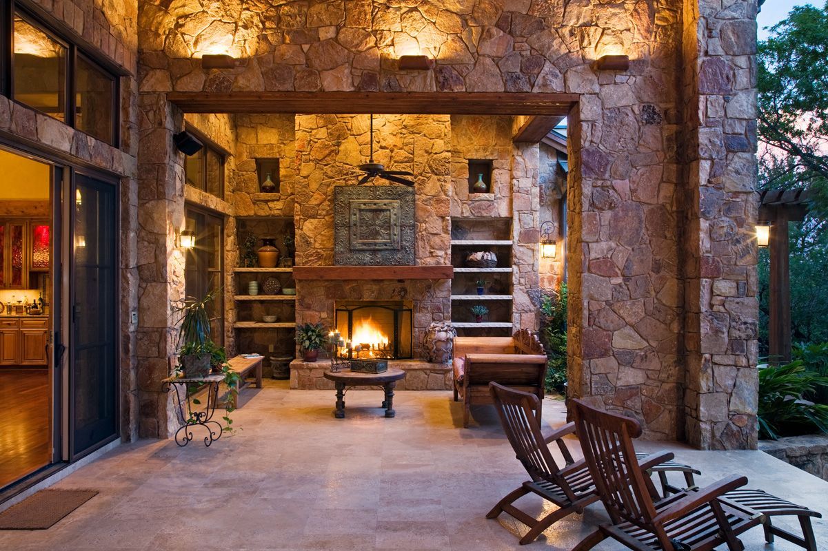 Patio with stone fireplace, wooden chairs, and warm lighting.