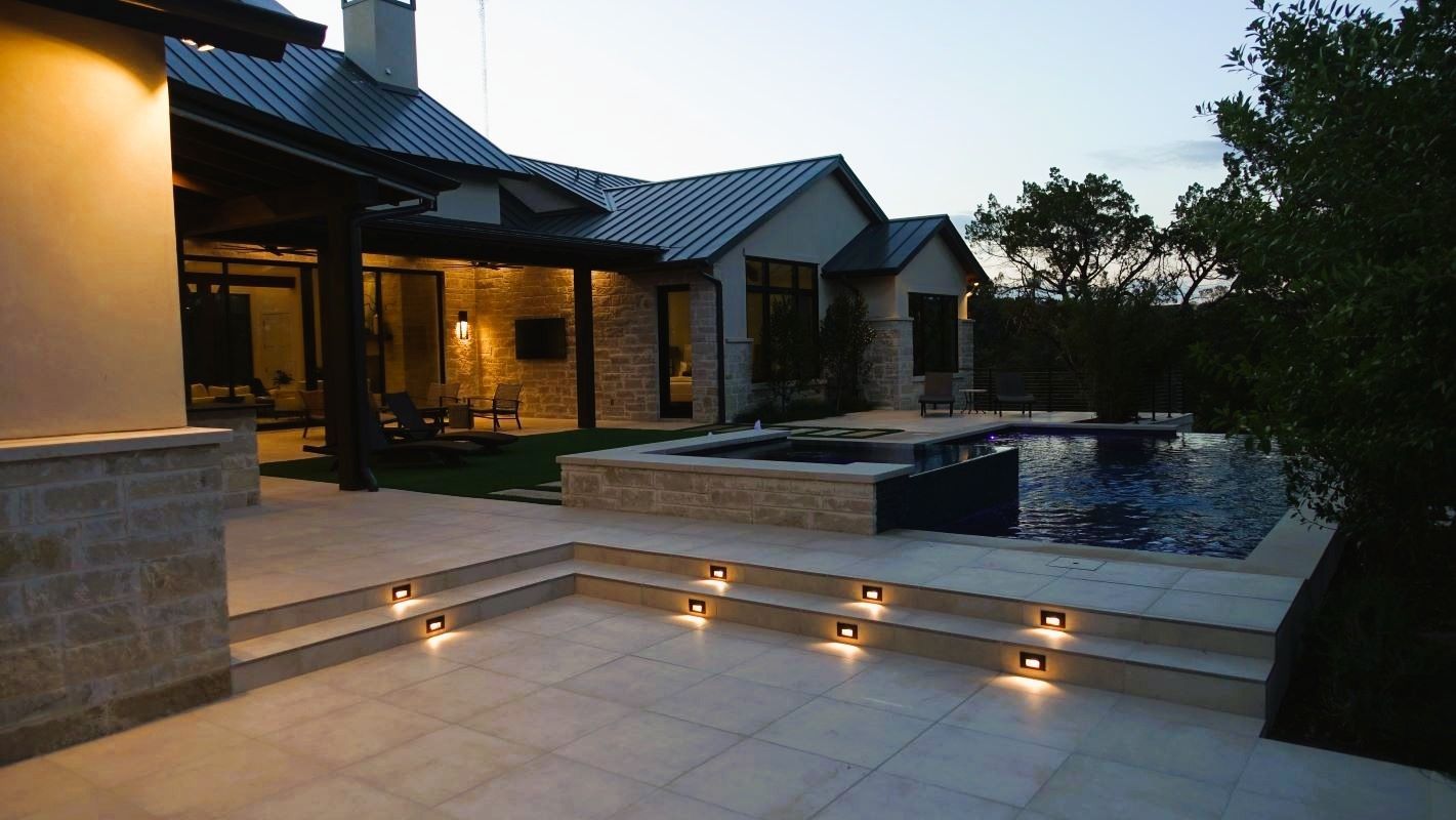 Patio with steps leading to pool and house at dusk, lit by soft lights.